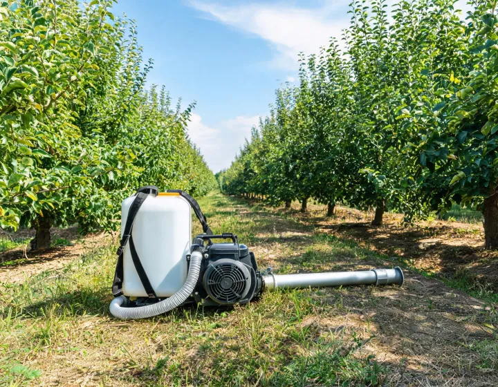 Backpack mist blower beside orchard rows